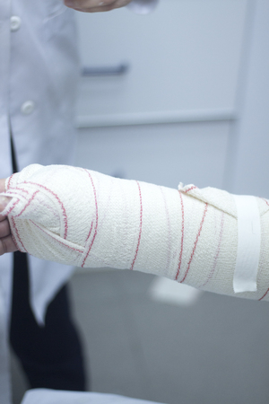 Doctor applying a plaster cast and bandages to patient forearm and wrist to immobilize after fracture injury.の写真素材