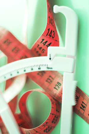 Fat caliper and measuring tape used to measure waistline, bodyfat levels for fitness and obesity checks.の写真素材