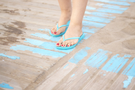 Lady's feet with red nail varnish in sandals on the sandy beach by the ocean in summer on wooden...