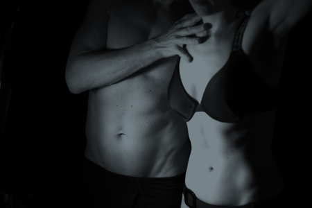 Sexy couple semi nude slim athletic man and erotic slender lady naked touching bodies in underwear in dark.の写真素材