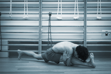 Male yoga teacher doing splits calisthenics and yoga asana practice in gym fitness pilates studio.