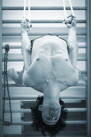 Male yoga teacher doing wall bars and ropes calisthenics and yoga asana practice in gym  pilates studio.の写真素材