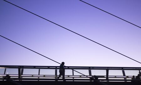 Person walking on modern architecture metal bridge in silhouette in evening dusk light.の写真素材