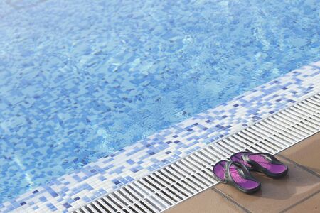 Blue swimming pool on hot sunny day on summer vacation and rubber sandals.