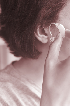 Deaf middle aged lady wearing modern digital high technology hearing aid in ear.の写真素材