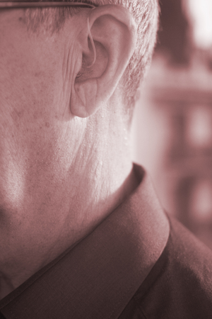Deaf senior citizen man wearing modern digital high technology hearing aid in ear.の写真素材
