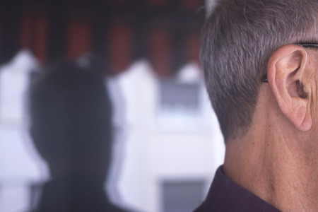 Deaf senior citizen man wearing modern digital high technology hearing aid in ear.の写真素材