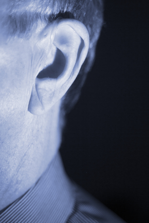 Deaf senior citizen man wearing modern digital high technology hearing aid in ear.の写真素材