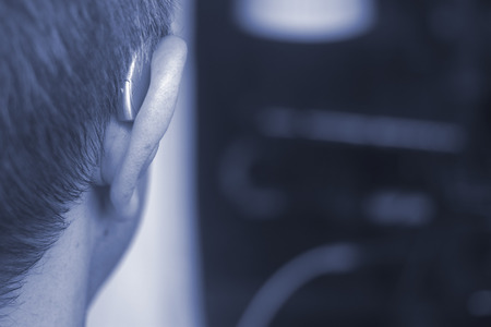 Deaf middle aged man wearing modern digital high technology hearing aid in ear.の写真素材