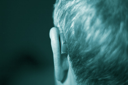 Deaf senior citizen man wearing modern digital high technology hearing aid in ear.の写真素材