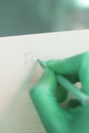 Young lady writing on paper with pencil in hand on table.の写真素材