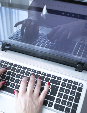 Secretary typist typing on laptop pc computer keyboard keys with hands with red nail varnish.
