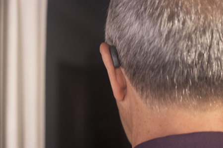 Deaf senior citizen man wearing modern digital high technology hearing aid in ear.