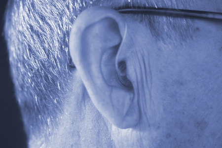 Deaf senior citizen man wearing modern digital high technology hearing aid in ear.