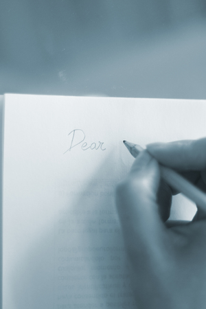 Young lady writing on paper with pencil in hand on table.の写真素材