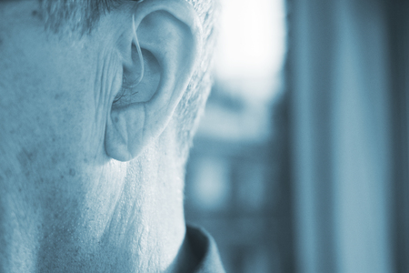 Deaf senior citizen man wearing modern digital high technology hearing aid in ear.の写真素材