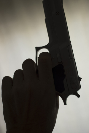 Pistol automatic handgun weapon in silhouette in hand of killer atmospheric dark dramatic photo.