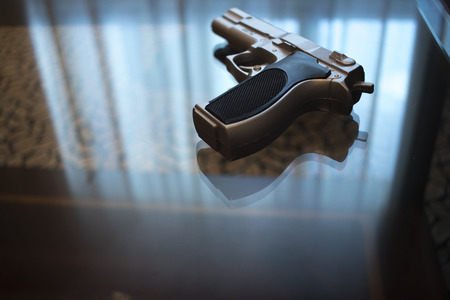 Automatic pistol gun on glass table in bedroom in luxury hotel in silhouette with reflection of...