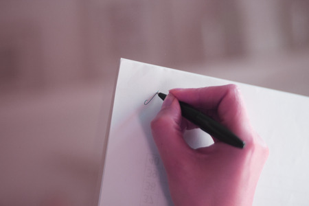 Young lady writing on paper with pencil in hand on table.の写真素材
