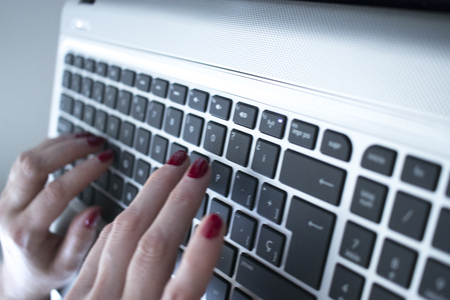 Secretary typist typing on laptop pc computer keyboard keys with hands with red nail varnish.
