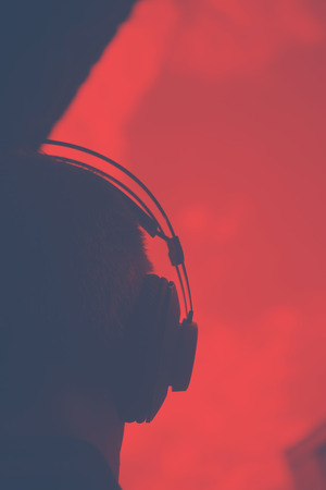 DJ deejay producer wearing closed headphones listening to music in artistic photo.