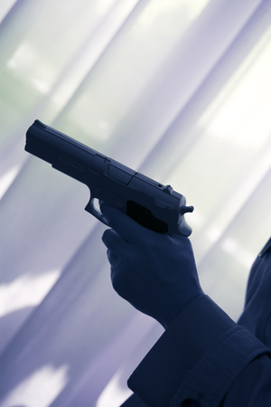 Hand holding automatic pistol gun in bedroom in luxury hotel in silhouette with window light.の写真素材