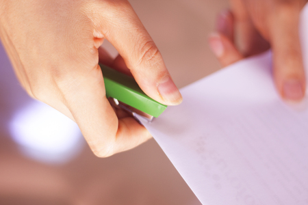 Office staple gun stapling paper in hand of young lady.の写真素材