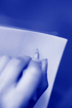 Young lady writing on paper with pencil in hand on table.の写真素材