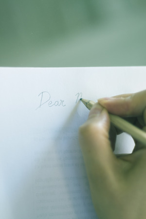 Young lady writing on paper with pencil in hand on table.の写真素材