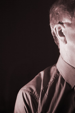 Deaf senior citizen man wearing modern digital high technology hearing aid in ear.の写真素材