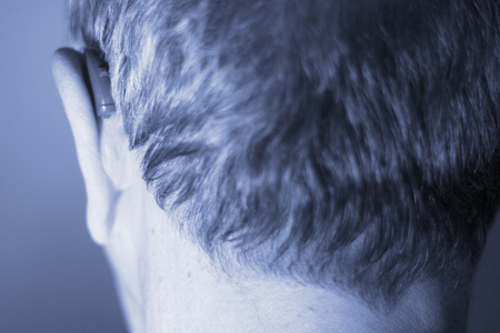Deaf senior citizen man wearing modern digital high technology hearing aid in ear.の写真素材