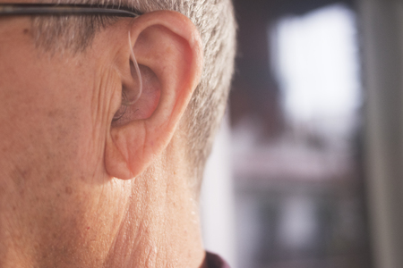 Deaf senior citizen man wearing modern digital high technology hearing aid in ear.