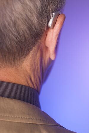 Caucasian white old aged man wearing modern digital hearing aid in ear with grey hair.の写真素材