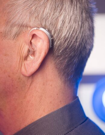 Caucasian white old aged man wearing modern digital hearing aid in ear with grey hair.の写真素材