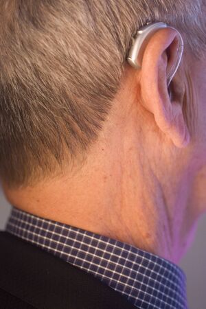 Caucasian white old aged man wearing modern digital hearing aid in ear with grey hair.の写真素材