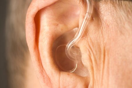 Caucasian white old aged man wearing modern digital hearing aid in ear with grey hair.