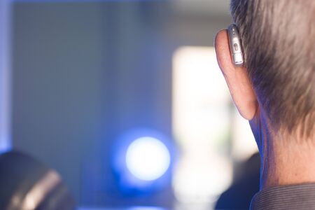 Caucasian white old aged man wearing modern digital hearing aid in ear with grey hair.