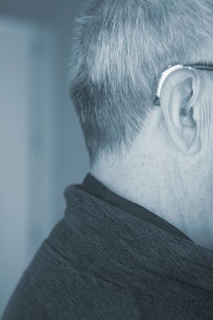 Caucasian white old aged man wearing modern digital hearing aid in ear with grey hair.の写真素材