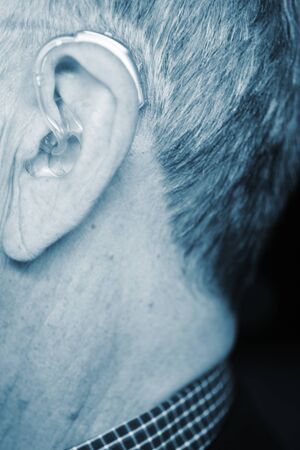 Caucasian white old aged man wearing modern digital hearing aid in ear with grey hair.の写真素材