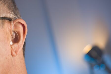 Caucasian white old aged man wearing modern digital hearing aid in ear with grey hair.