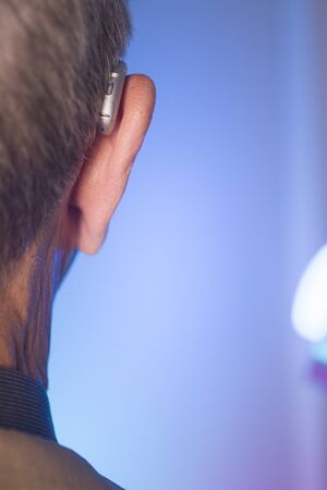 Caucasian white old aged man wearing modern digital hearing aid in ear with grey hair.の写真素材