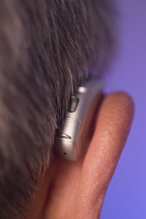 Caucasian white old aged man wearing modern digital hearing aid in ear with grey hair.