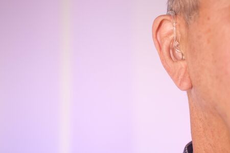 Caucasian white old aged man wearing modern digital hearing aid in ear with grey hair.