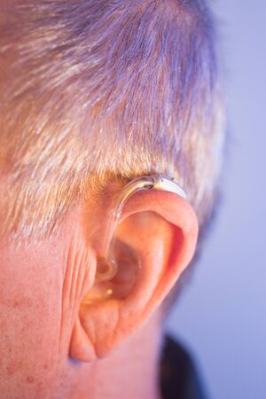 Caucasian white old aged man wearing modern digital hearing aid in ear with grey hair.