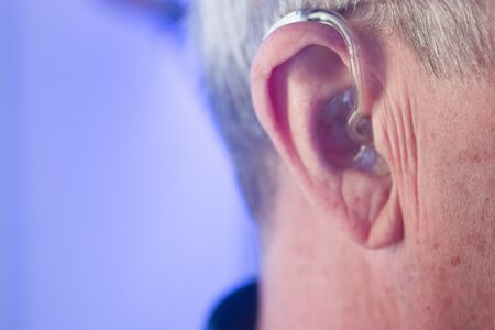 Caucasian white old aged man wearing modern digital hearing aid in ear with grey hair.