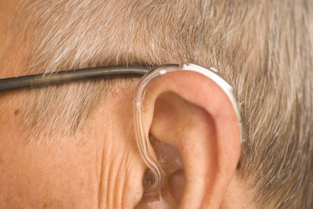 Caucasian white old aged man wearing modern digital hearing aid in ear with grey hair.の写真素材