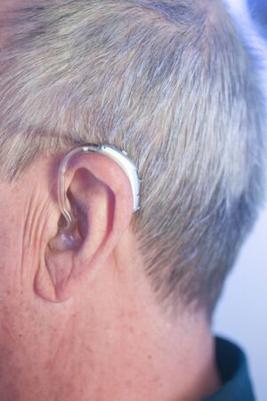 Caucasian white old aged man wearing modern digital hearing aid in ear with grey hair.の写真素材