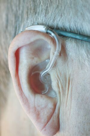 Caucasian white old aged man wearing modern digital hearing aid in ear with grey hair.の写真素材