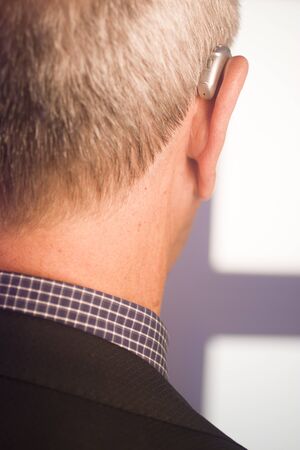 Caucasian white old aged man wearing modern digital hearing aid in ear with grey hair.の写真素材