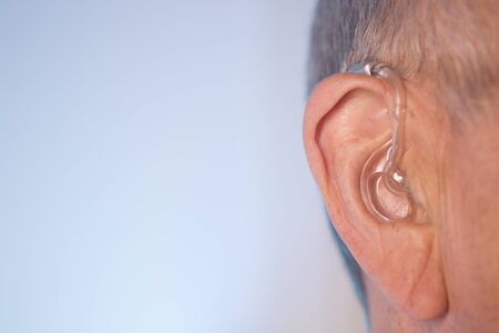 Caucasian white old aged man wearing modern digital hearing aid in ear with grey hair.の写真素材